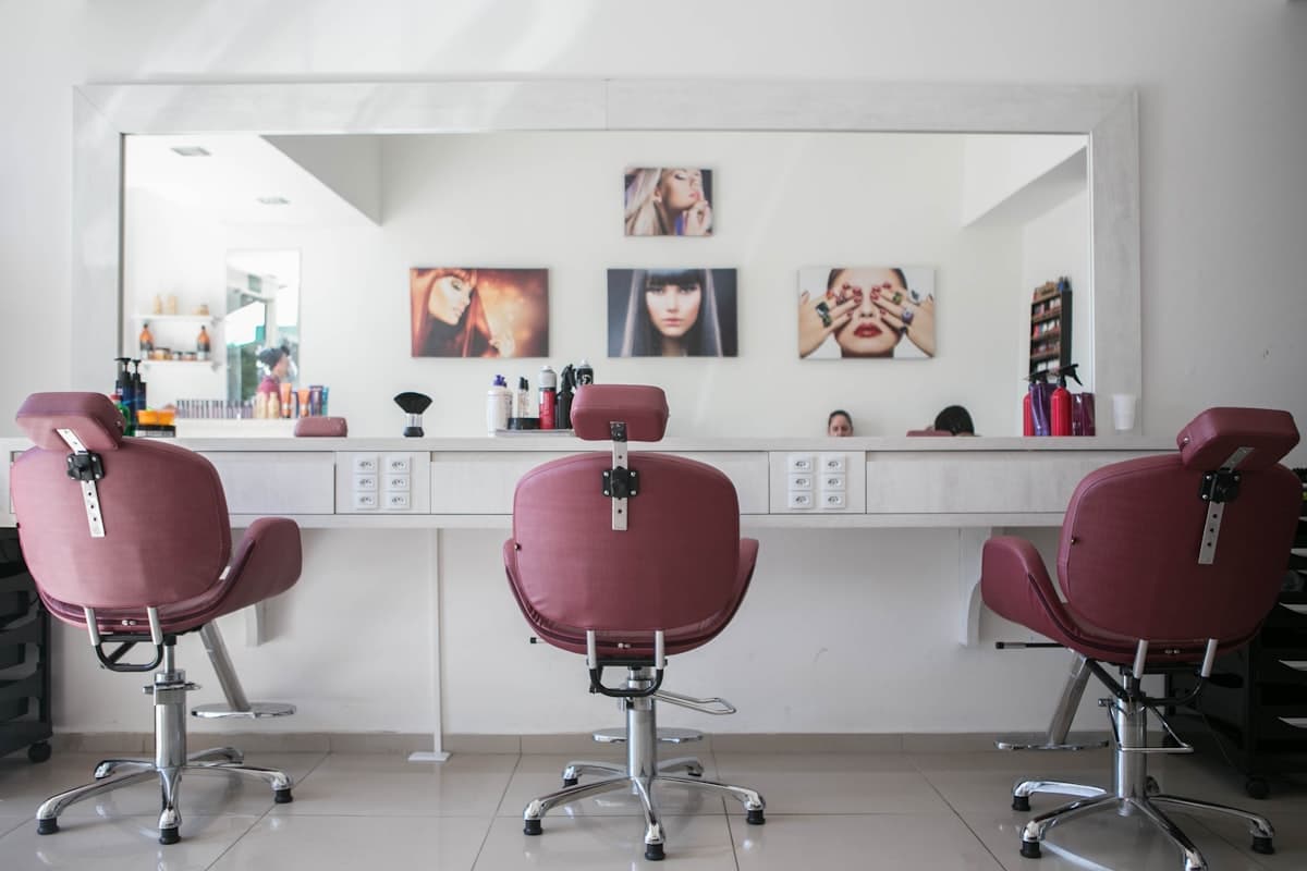 Drei leere Friseurstühle vor einem großen Spiegel im Salon
